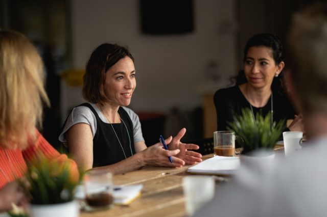 Plusieurs femmes en petit groupe discutent autour d'un café debout.