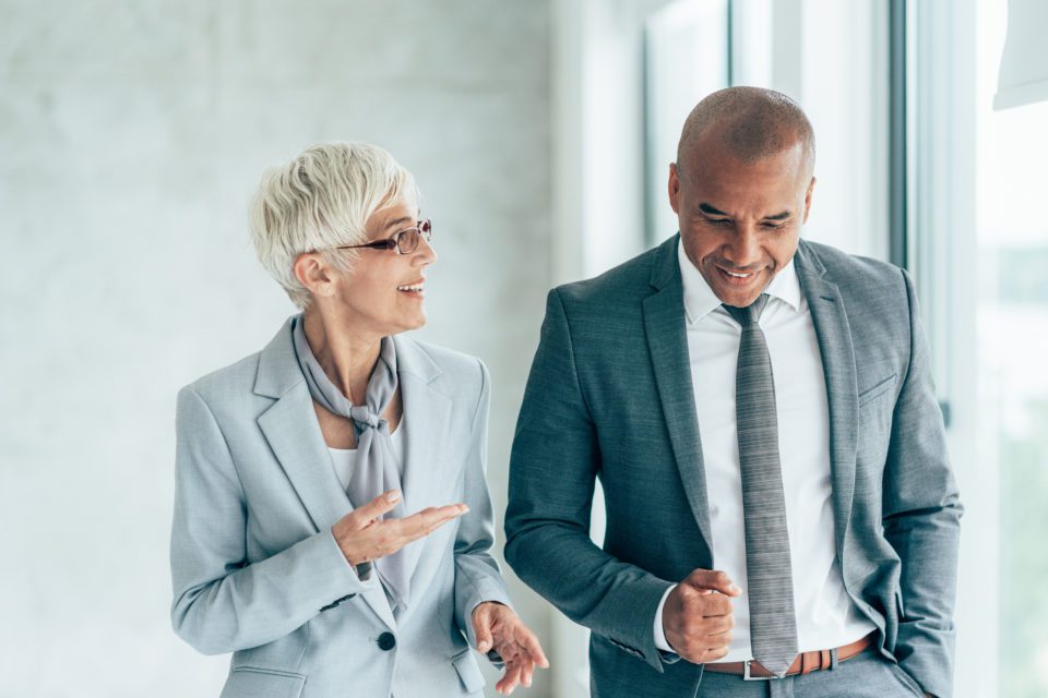 White mature corporate woman talking to a black man with a tie