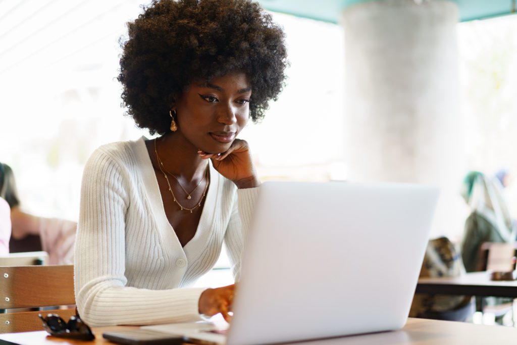 Jeune femme active noire, regardant et souriant à son ordinateur portable en lisant l'accompagnement offert par L'effet A à ses partenaires corporatifs qui mettent la parité au coeur de leur développement stratégique d'entreprise.